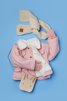 Dziecięca różowa futrzana kurtka z szalikiem i uroczą torbą na niebieskim tle. stylowa odzież wierzchnia dla dzieci. zimowy strój mody