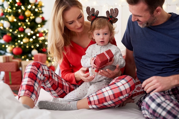 Dziecko otwierające świąteczny prezent z rodzicami w łóżku
