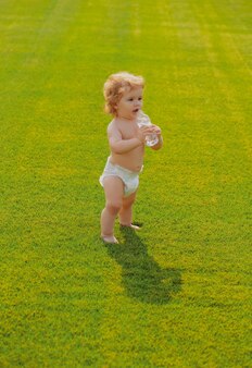 Dziecko pije czystą wodę z butelki na świeżym powietrzu na wiosennym zielonym polu zdrowe dziecko