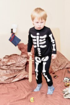 Dziecko w stroju szkieleta z drewnianym mieczem bawi się na kanapie