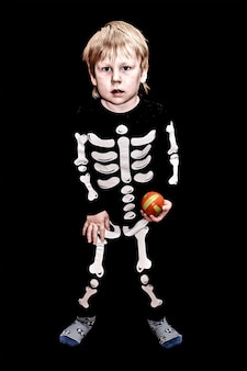 Dziecko w stroju szkieleta z pomarańczową kulką w ręku na czarnym tle