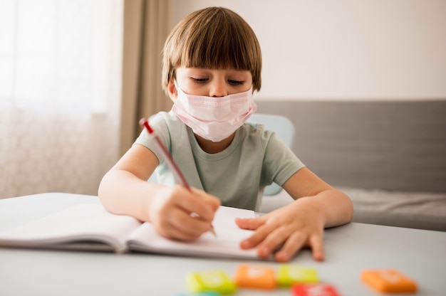 Dziecko z medyczną maską pisze przy biurkiem