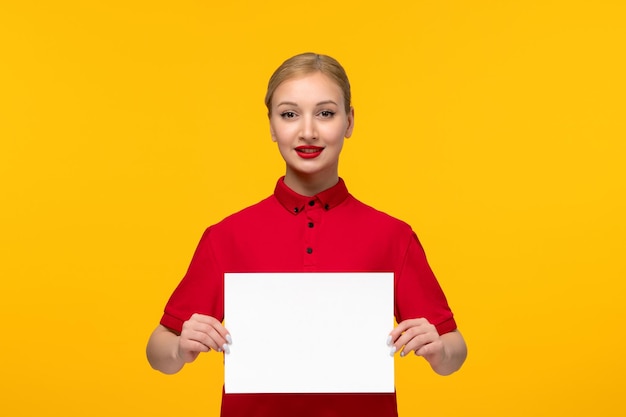 Bezpłatne zdjęcie dzień czerwonej koszuli śliczna blondynka trzymająca biały papier w czerwonej koszuli na żółtym tle