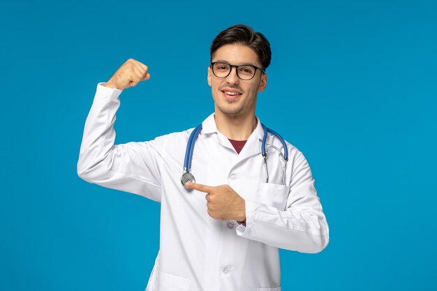 Dzień lekarza przystojny brunet ładny facet w sukni medycznej pokazując biceps off