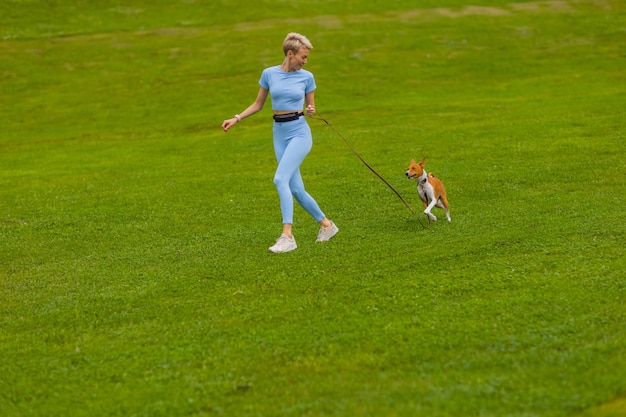 Dziewczyna biegnie z psem w parku na trawniku o zachodzie słońca, spacery zwierzaka w przyrodzie.