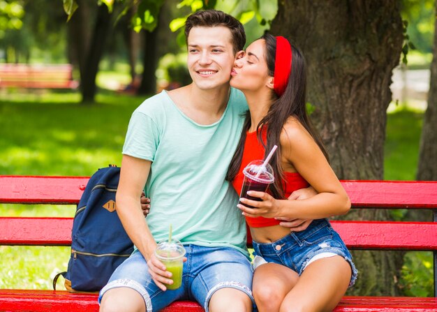 Dziewczyna całuje jej chłopaka gospodarstwa koktajle w plastikowej filiżanki