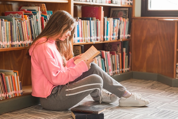 Bezpłatne zdjęcie dziewczyna czyta blisko bookcase