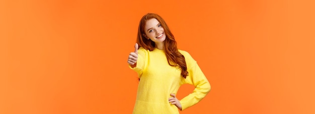 Bezpłatne zdjęcie dziewczyna dająca pozwolenie mówi tak, wesoła ruda kobieta w żółtym swetrze wyciąga rękę i pokazuje kciuk do góry
