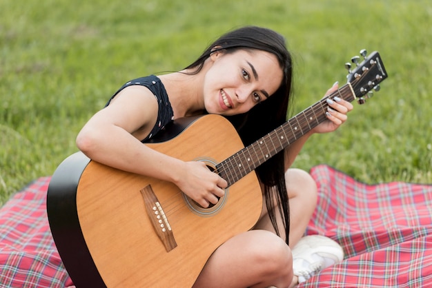Bezpłatne zdjęcie dziewczyna gra na gitarze na koc piknikowy