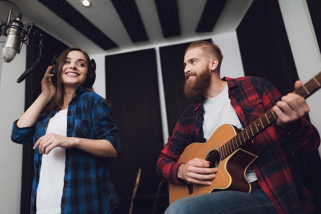 Dziewczyna i facet śpiewają piosenkę na gitarę w nowoczesnym studiu nagrań