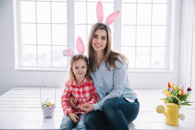 Dziewczyna i matka w uszy królika siedzi w pobliżu kosz z kolorowych jaj