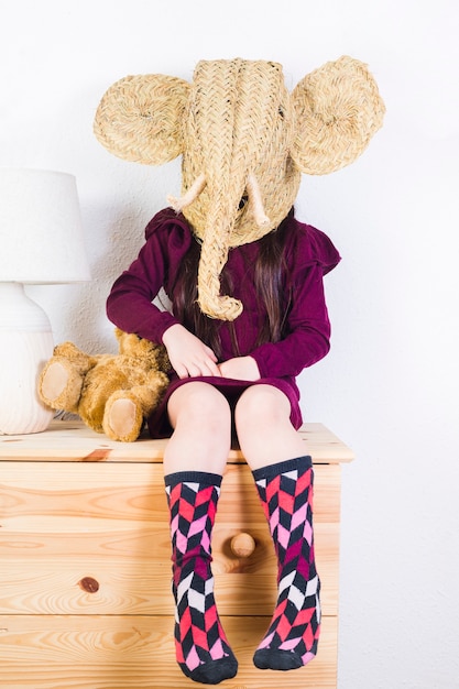 Dziewczyna jest ubranym łozinowego słonia maskowego obsiadanie na stole