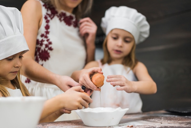 Dziewczyna pęka jajko w pucharze podczas gdy przygotowywający jedzenie