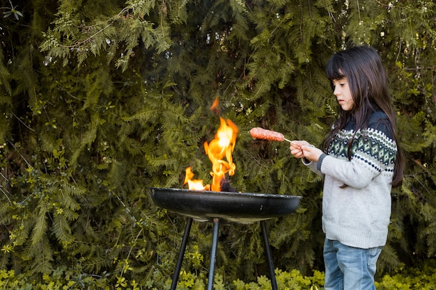 Bezpłatne zdjęcie dziewczyna piec na grillu kiełbasy na plenerowym grillu