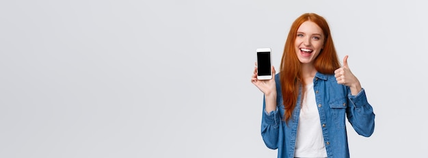 Bezpłatne zdjęcie dziewczyna pokazuje przyjacielowi fajną nową grę mobilną atrakcyjną wesołą rudą kobietę trzymającą smartfona