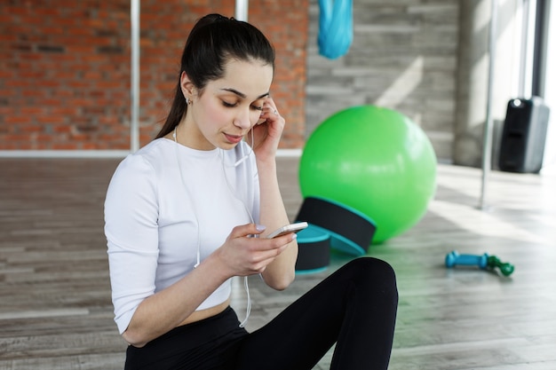 Dziewczyna pracuje ze swoim smartfonem po treningu lub przed treningiem na siłowni