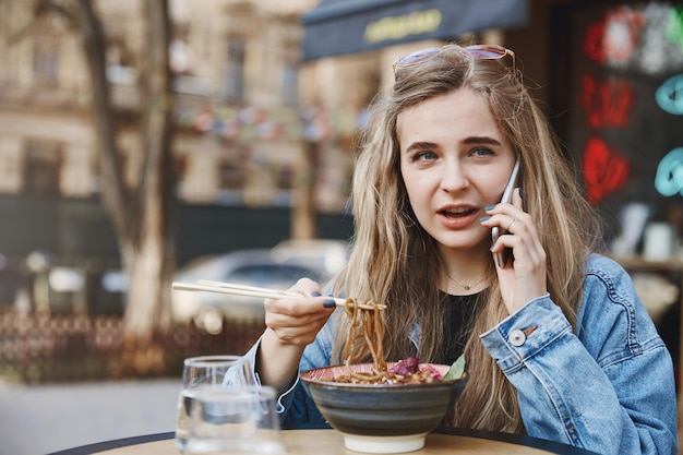 Bezpłatne zdjęcie dziewczyna prowadząca przyjaciela przez smartfona jedząca w azjatyckiej restauracji a