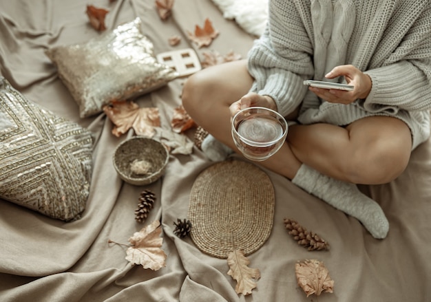 Dziewczyna robi zdjęcie filiżanki herbaty wśród jesiennych liści, jesienna kompozycja.