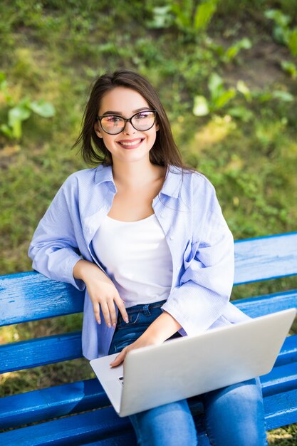 Dziewczyna siedzi na ławce w parku i korzysta z laptopa