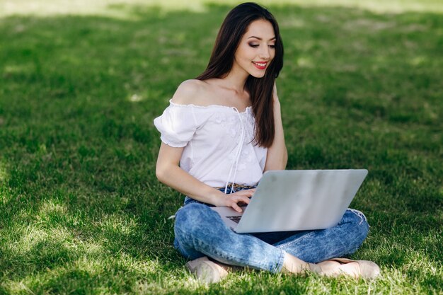 Dziewczyna siedzi w parku, wpisując na swoim laptopie