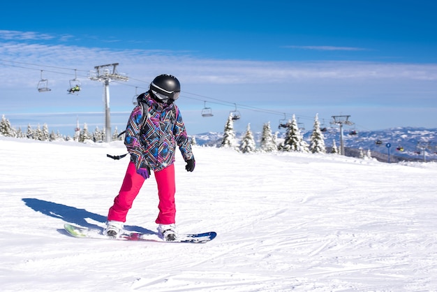 Dziewczyna uczy się jazdy na snowboardzie w górskim kurorcie z wyciągiem narciarskim w tle