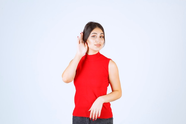 Dziewczyna w czerwonej koszuli wskazując jej ucho, aby dobrze słyszeć.