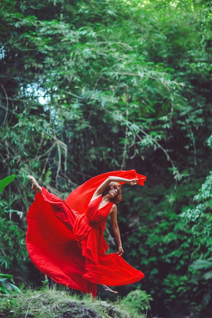 Dziewczyna w czerwonej sukience tańczy w wodospadzie.
