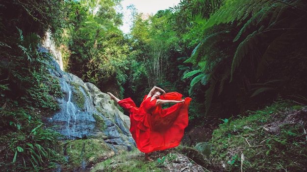 Dziewczyna w czerwonej sukience tańczy w wodospadzie.