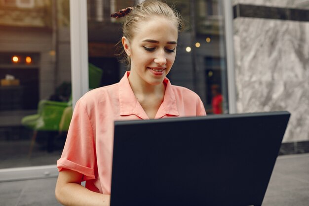 Dziewczyna w różowej koszuli siedzi w pobliżu domu i korzysta z laptopa