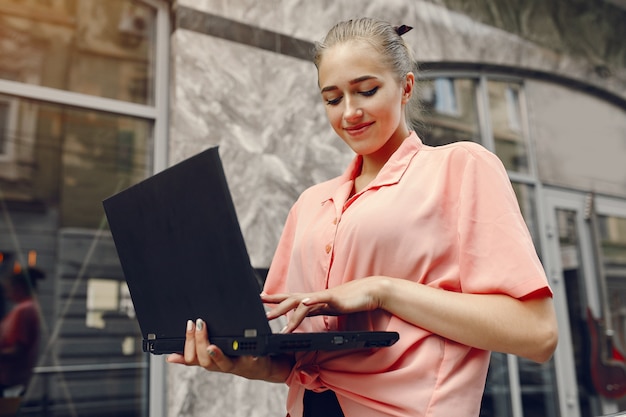 Dziewczyna w różowej koszuli siedzi w pobliżu domu i korzysta z laptopa