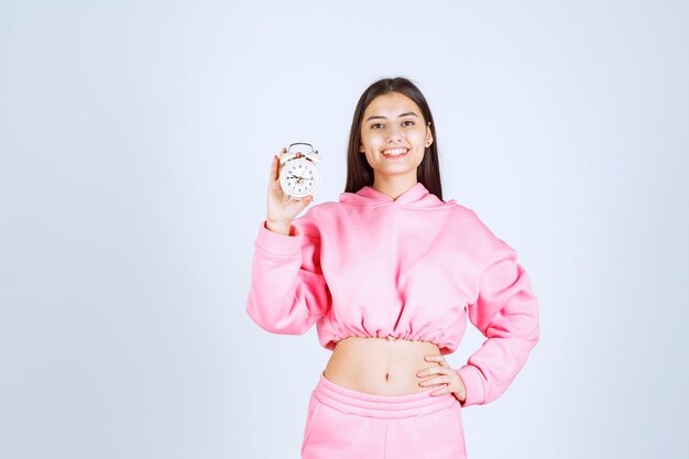 Dziewczyna w różowej piżamie trzymająca budzik i promująca go jako produkt.