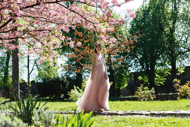 Dziewczyna w różowej sukience stoi pod kwitnącym drzewem sakura w parku