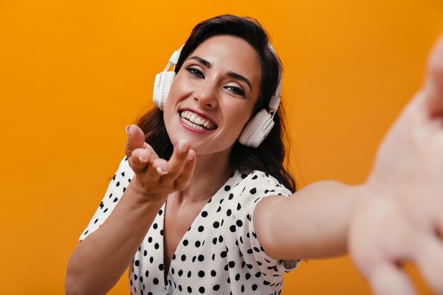 Dziewczyna w świetnym nastroju słucha muzyki w słuchawkach i bierze selfie na pomarańczowym tle