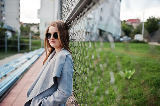 Dziewczyna w szarym płaszczu z okularami przeciwsłonecznymi na małym stadionie ulicznym
