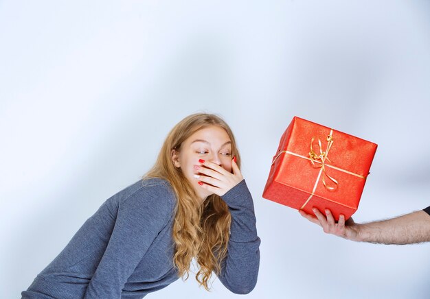 Dziewczyna wygląda na zaskoczoną, gdy dostaje czerwone pudełko na prezent.