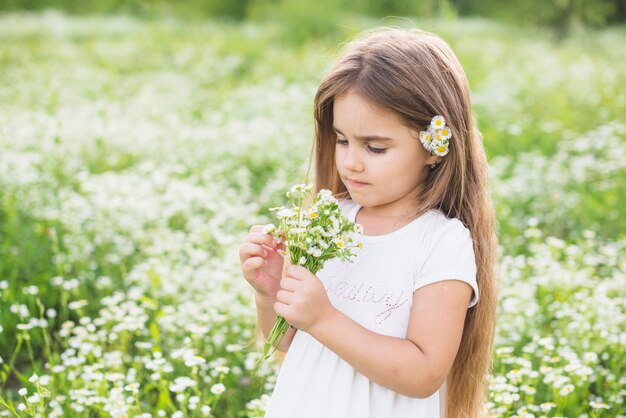 Dziewczyna z długimi włosami patrząc na białe kwiaty zebrane przez nią w polu