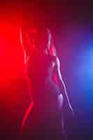 Bezpłatne zdjęcie dziewczyna z idealną szczupłą sylwetką. kobieta pozuje w body w czerwonym świetle w dymie.
