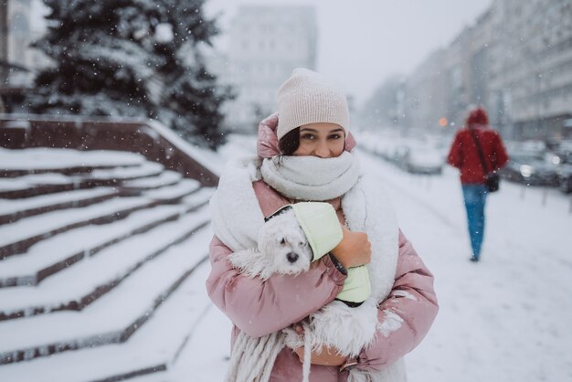 Dziewczyna z psem na rękach na ulicy miasta pada śnieg