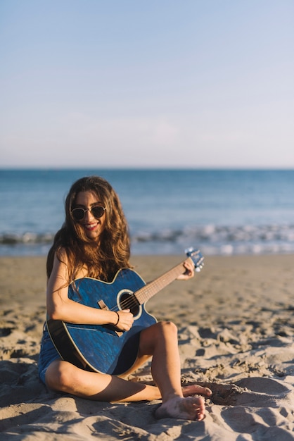 Dziewczynka gra na gitarze siedzi na piasku