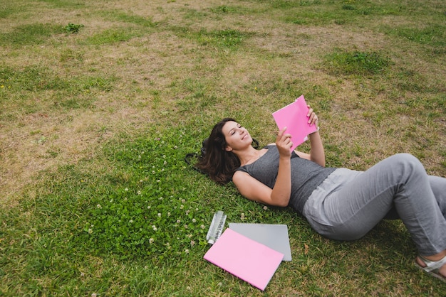 Bezpłatne zdjęcie dziewczynka leżącego na trawie czytania notebooka