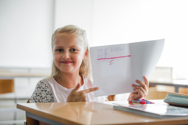 Bezpłatne zdjęcie dziewczynka siedzi w tabeli szkolnej z notebooka