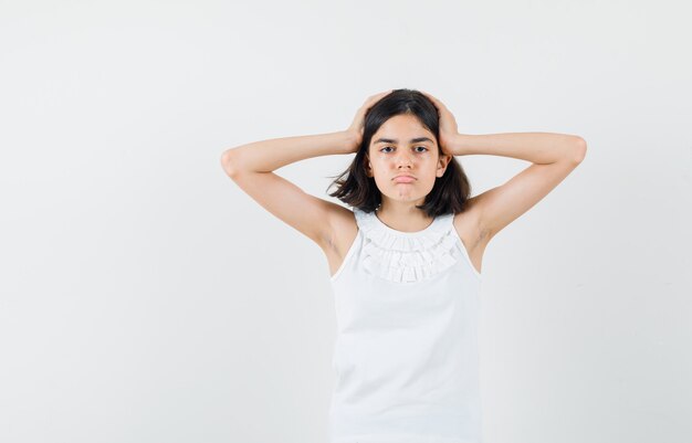 Dziewczynka trzymając się za ręce na głowie w białej bluzce i patrząc zmęczony, widok z przodu.