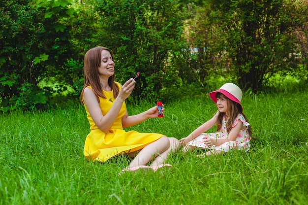 Dziewczynka uśmiecha, podczas gdy jej matka wieje Bańki mydlane