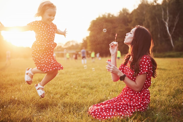 Bezpłatne zdjęcie dziewczynka z bąbelkami z matką w parku o zachodzie słońca.