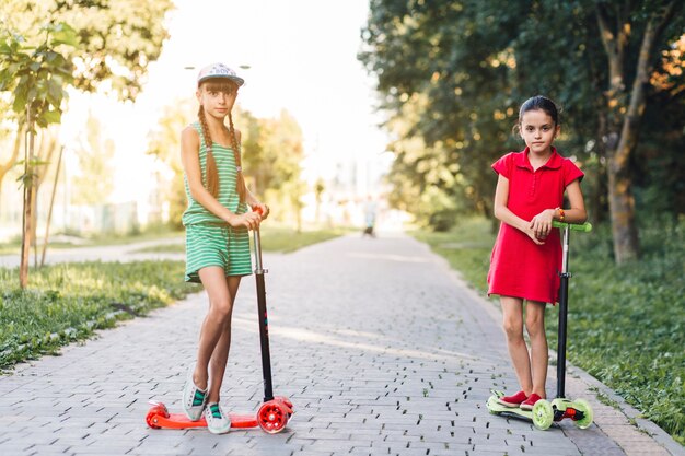 Dziewczynki stojące z hulajnogą na chodniku