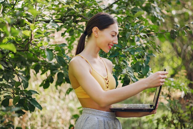 Dziewczyny pozycja w lato parku i mienie laptop w ona ręki