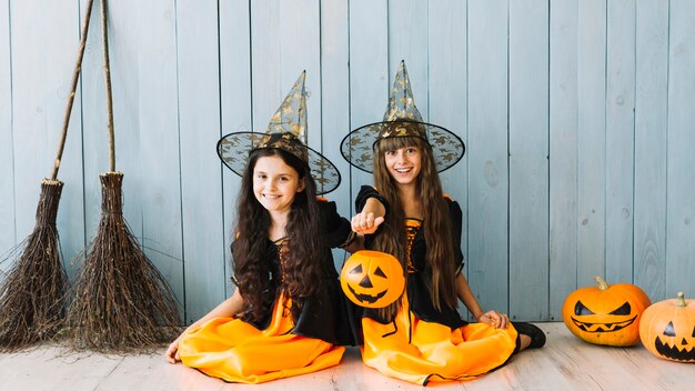 Dziewczyny w czarownicach garnitury siedzi na podłodze trzymając kosz Halloween i uśmiechając się