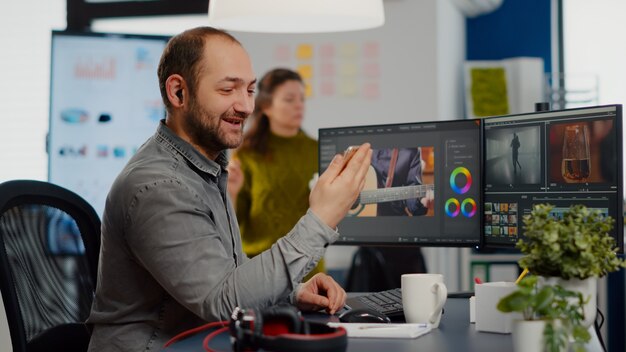 Edytor wideo rozmawiający podczas rozmowy wideo, trzymający edycję filmu na smartfonie, siedzący w uruchomionym agencie twórczym...