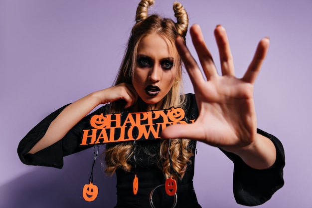 Bezpłatne zdjęcie ekstatyczna modelka przygotowuje się na halloween w studio przystojna dziewczyna z przerażającym makijażem pozuje na fioletowym tle