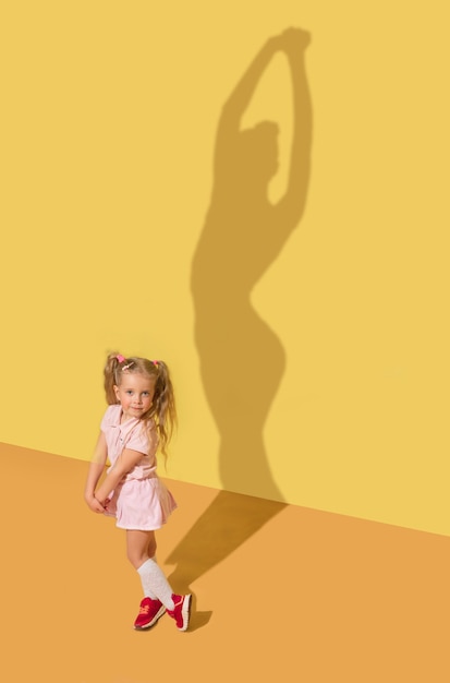 Bezpłatne zdjęcie elastyczność i sławę. koncepcja dzieciństwa i marzeń. obraz koncepcyjny z dzieckiem. cień na ścianie pracowni jest namalowany przeze mnie. mała dziewczynka chce zostać baletnicą, tancerką baletową, artystką teatru.